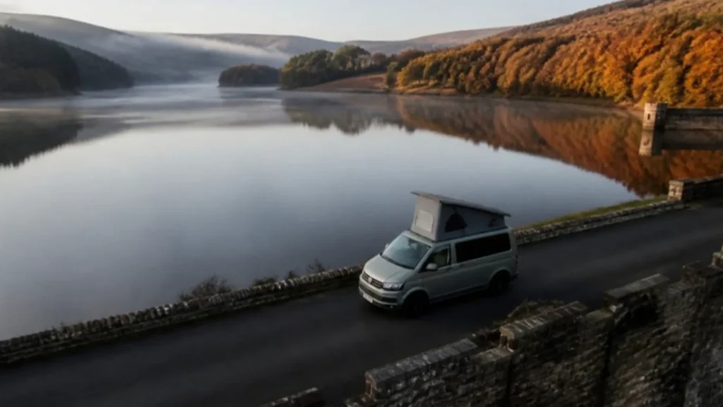 Silver pop top campervan on a road beside a misty reservoir with autumn trees