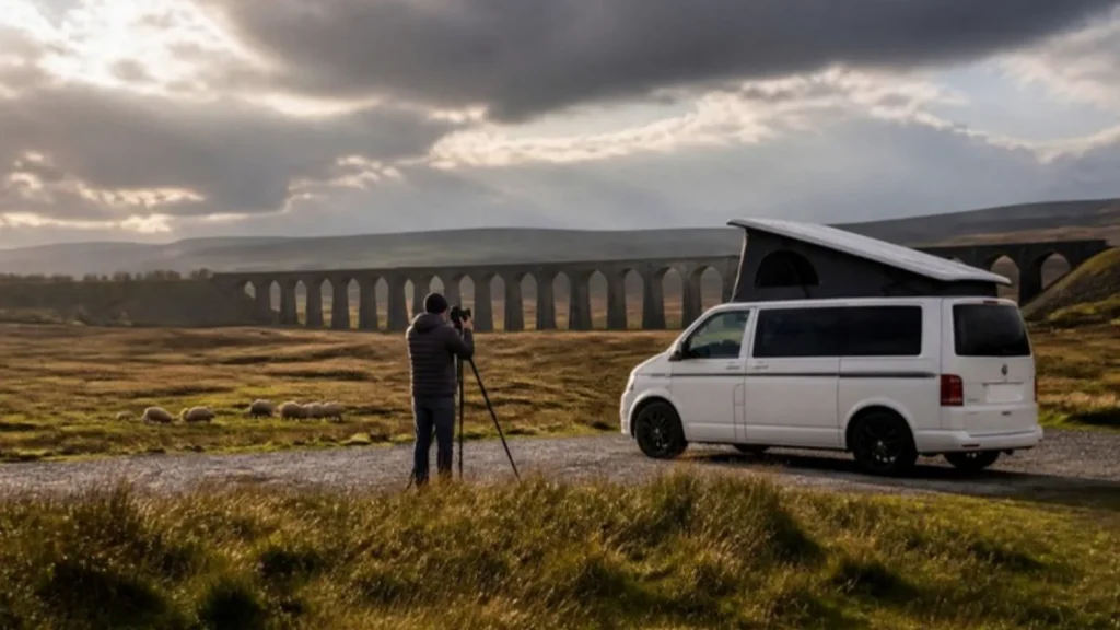 Photographer with a tripod next to a white pop top campervan in front of Ribblehead Viaduct