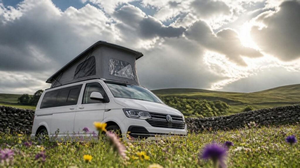 White VW T6.1 campervan with pop top roof raised in a wildflower meadow